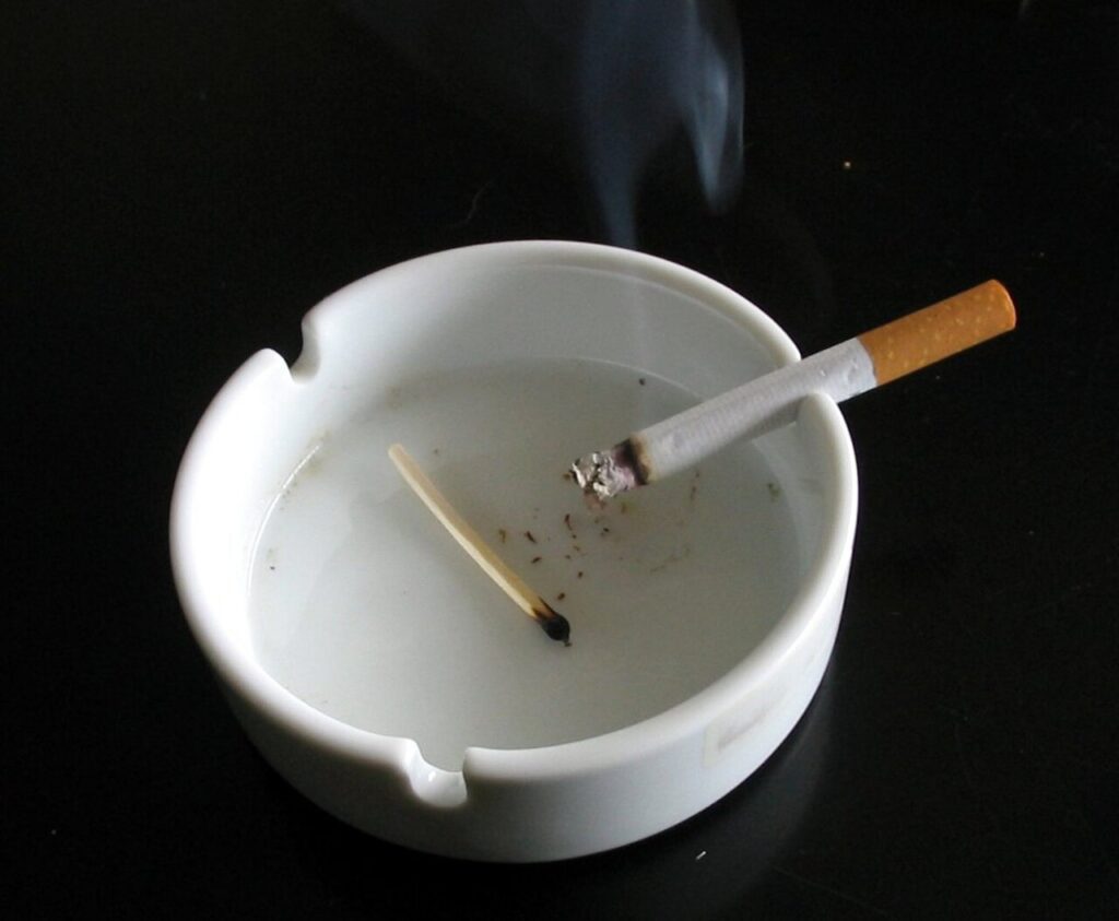 Un cigarrillo encendido en un cenicero blanco